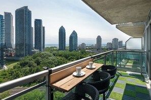 A balcony with a table and chairs, overlooking a cityscape with tall buildings and greenery. - Lakefront Oasis Modern 1BR w Den (Toronto)