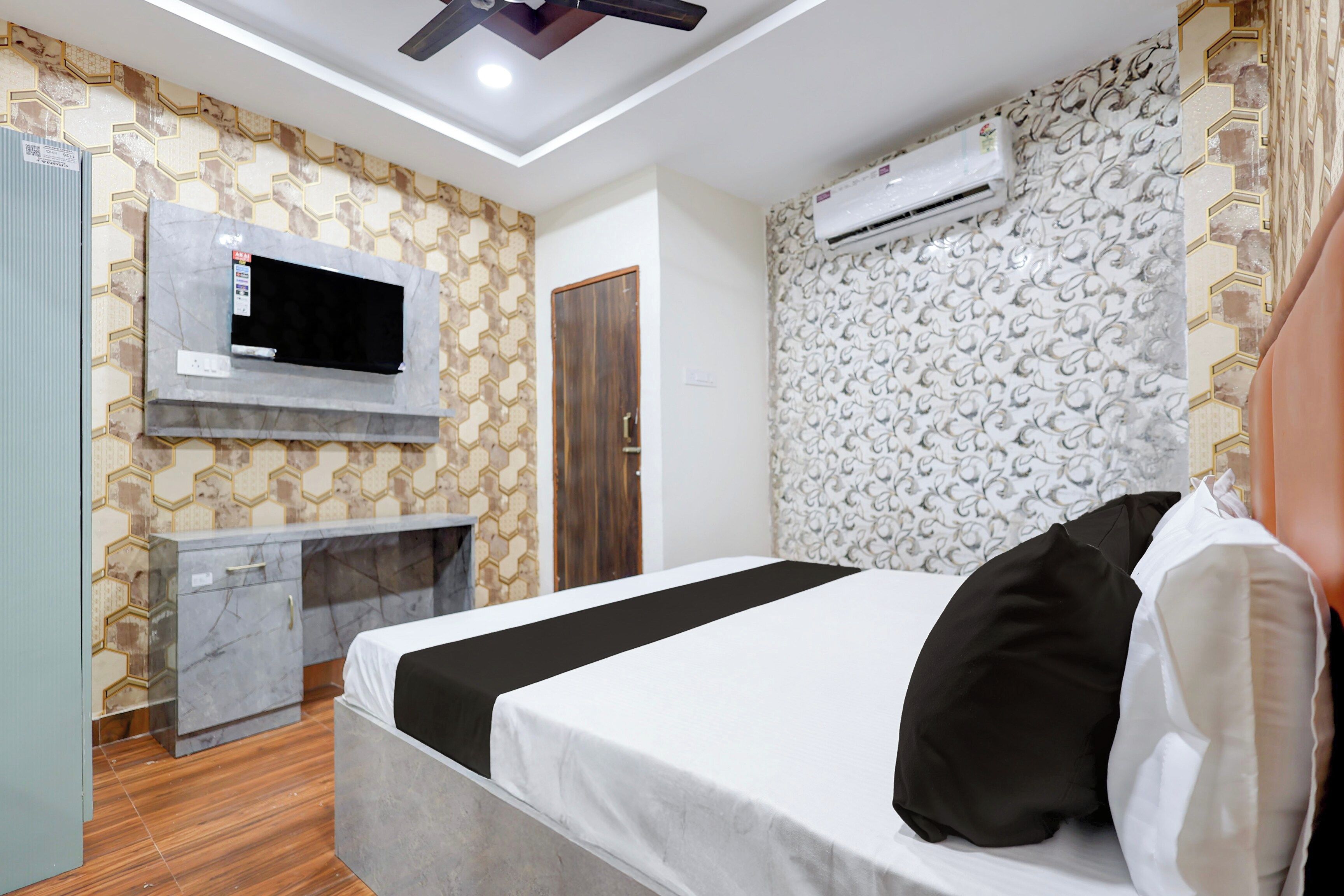A hotel room with a bed, a TV mounted on the wall, a wardrobe, and an air conditioning unit.