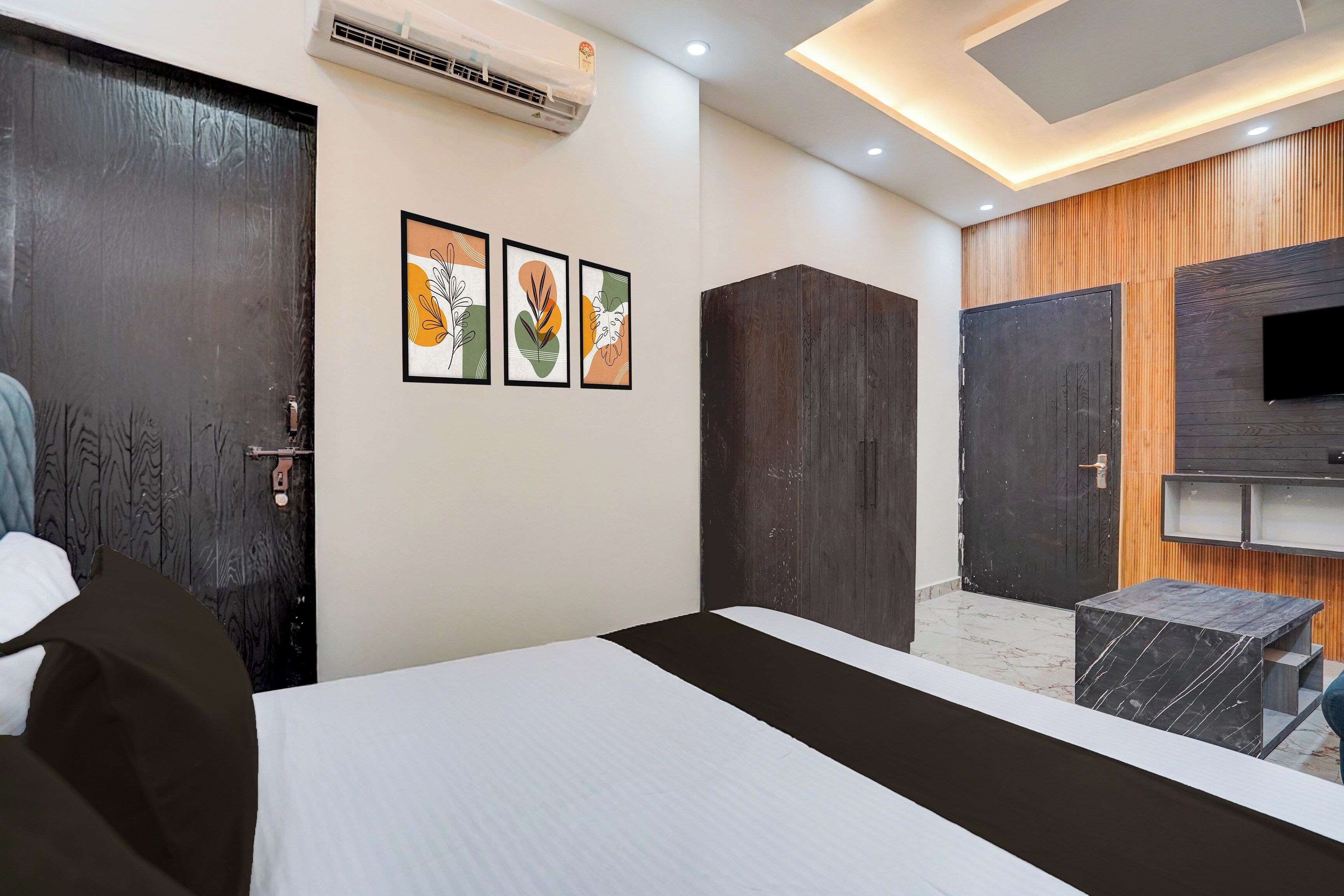 A hotel room with a bed, a TV, and a wall-mounted air conditioner.