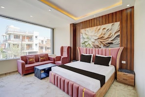 A modern bedroom with a large bed, a sofa, and a view of buildings outside. - Hotel O J K Galaxy Hotel (Kanpur)