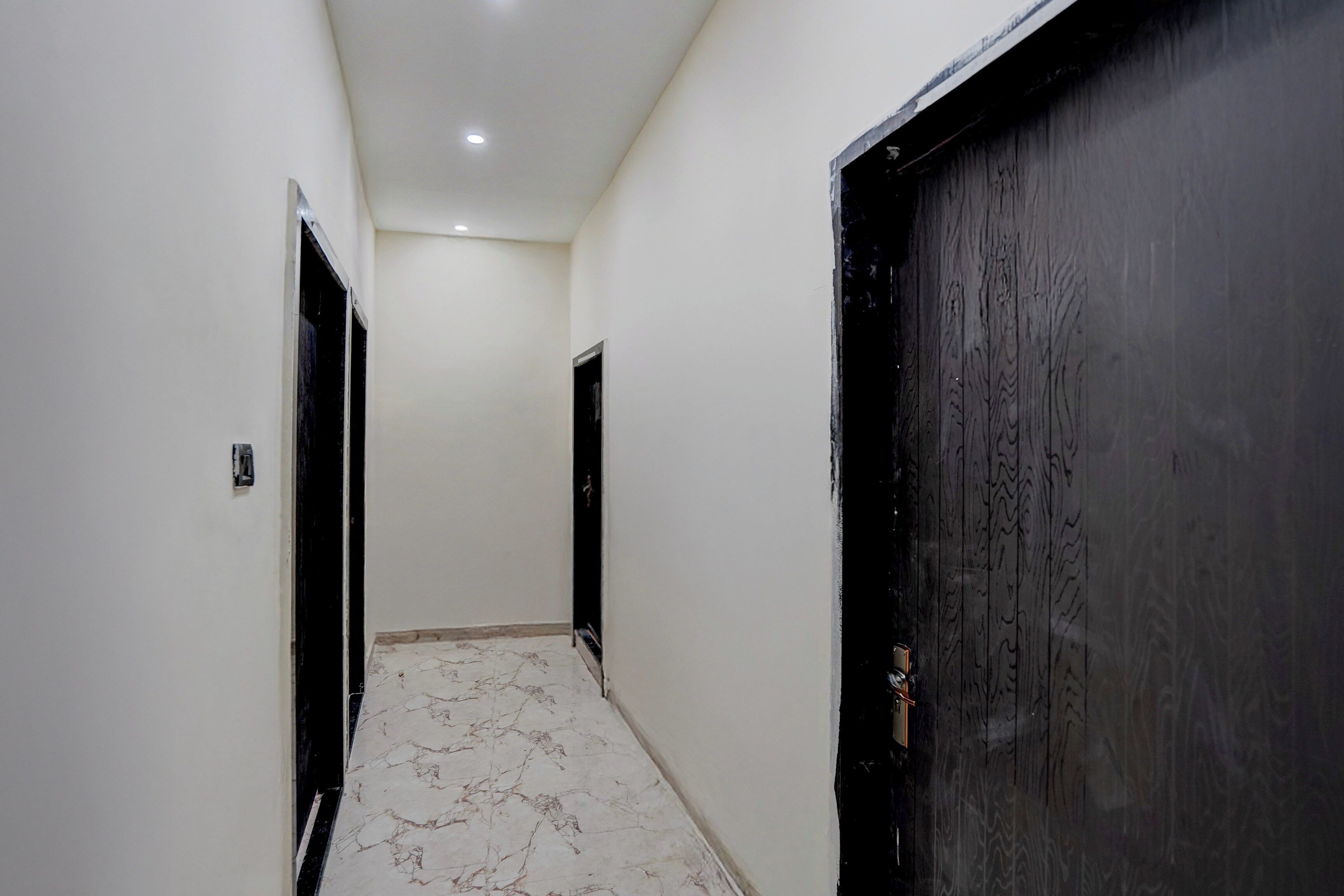 Un pasillo con paredes blancas, piso de mármol y dos puertas negras.