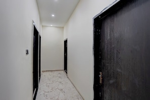 A hallway with white walls, a marble floor, and two black doors. - Hotel O J K Galaxy Hotel (Kanpur)