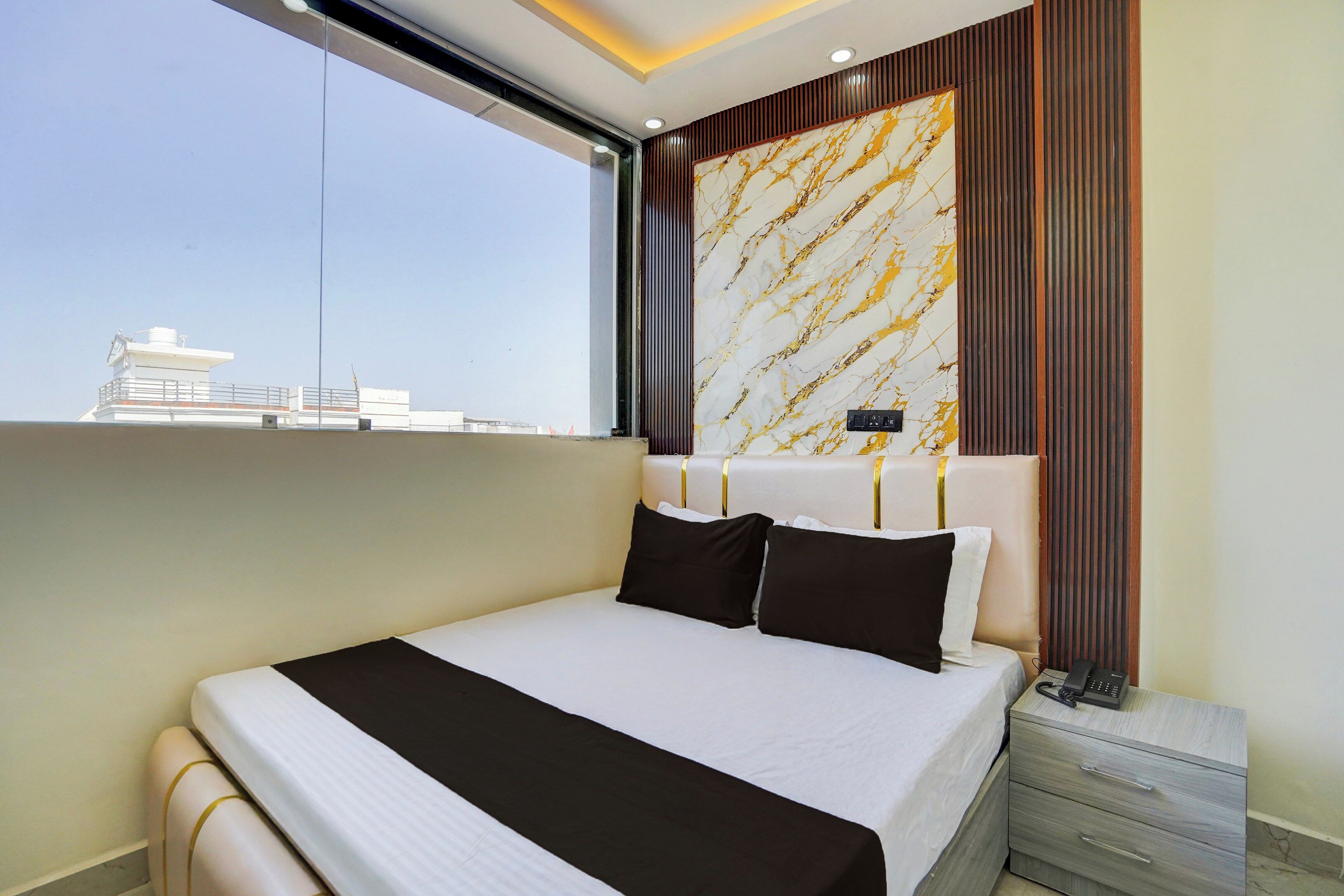 Habitación de hotel con una cama grande, una mesita de noche, un teléfono y vista a la ciudad.