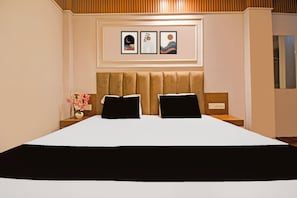 Une chambre d’hôtel avec un grand lit, deux oreillers, une table de chevet ornée d’un vase de fleurs et trois tableaux encadrés accrochés au mur.