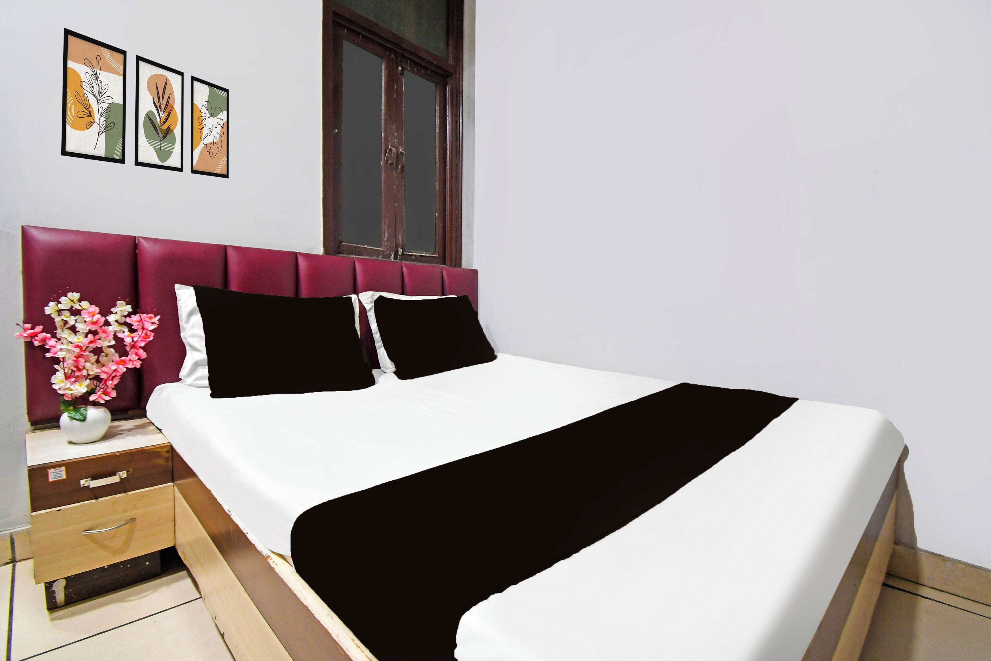 A hotel room with a bed, a nightstand, a vase with flowers, and three framed pictures on the wall.