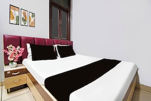 Une chambre d’hôtel avec un lit, une table de chevet, un vase de fleurs et trois tableaux encadrés accrochés au mur.