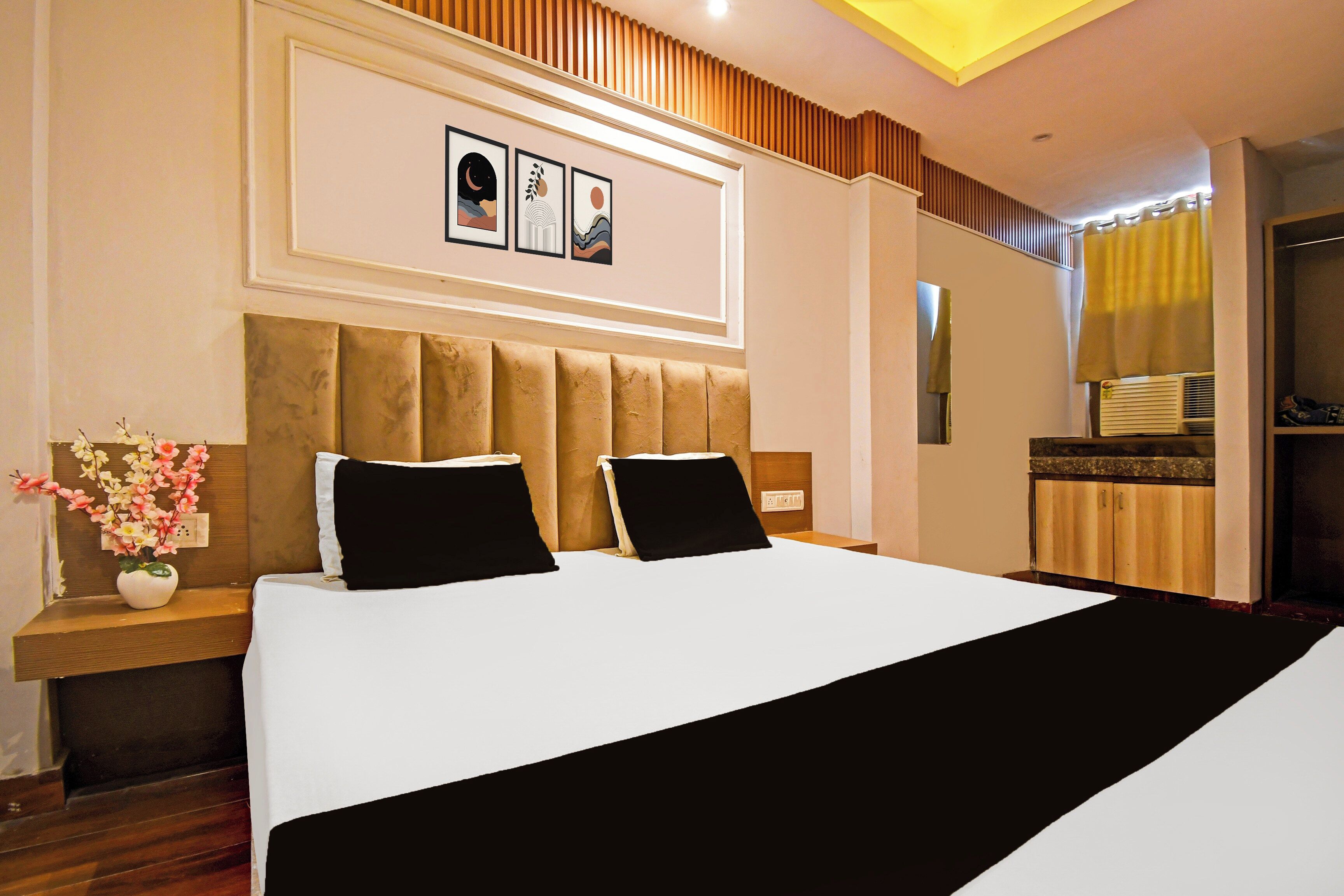 A hotel room with a large bed, a nightstand with a vase of flowers, and a wall-mounted artwork.