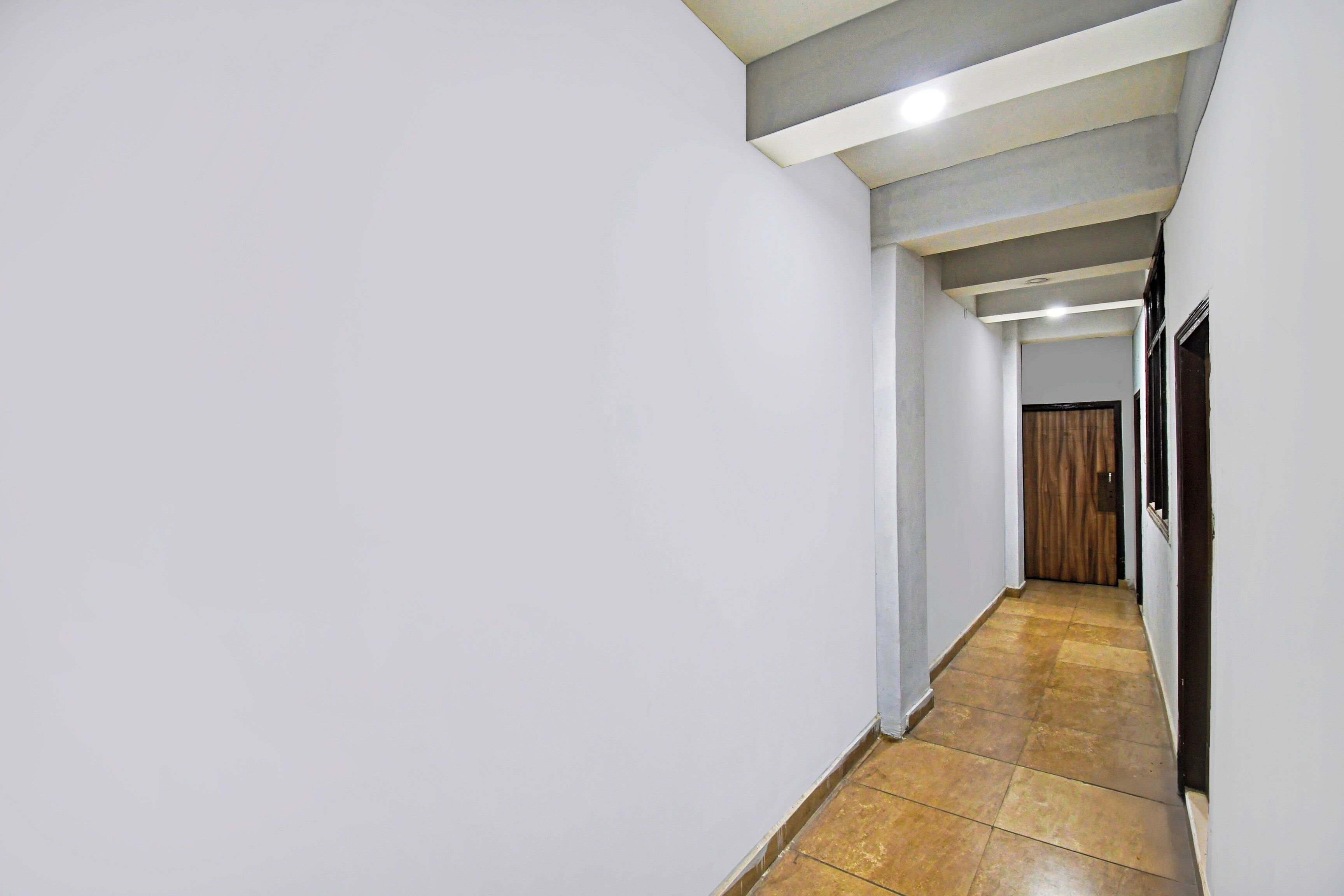 A narrow, tiled hallway with white walls and a wooden door at the end.
