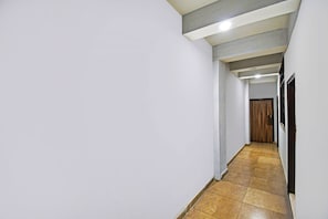Um corredor estreito, com piso de azulejos, paredes brancas e uma porta de madeira no final.