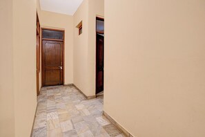 A narrow hallway with a wooden door at the end, tiled flooring, and plain walls. - Hotel O Ruchi Guest House (Kanpur)