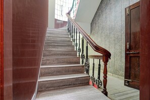 A staircase with a wooden handrail and metal balusters, leading to a door with a metal handle. - Hotel O Ruchi Guest House (Kanpur)