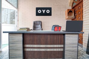 Een receptiebalie met een bord waarop 'OYO' staat, een lederen stoel, een laptop en een rood voorwerp op de balie.
