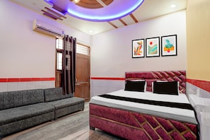 Een slaapkamer met een bed, een bank, een deur en drie ingelijste kunstwerken aan de muur.