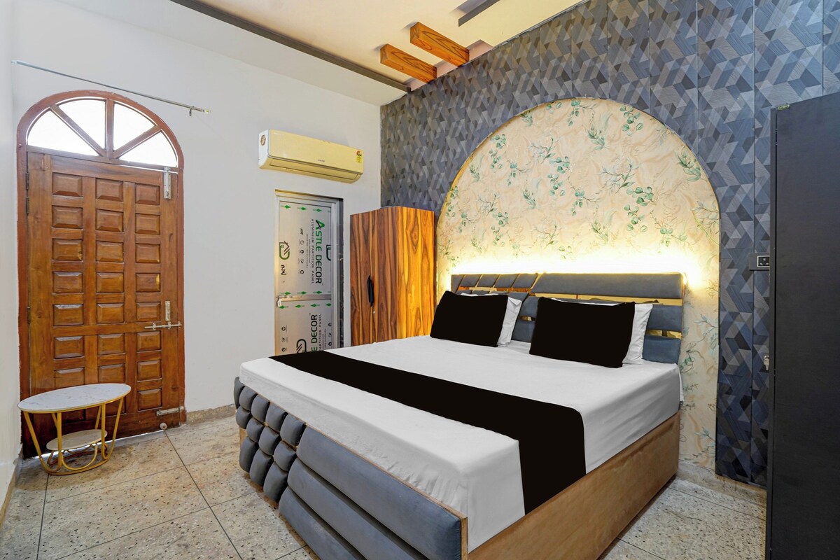 A bedroom with a bed, a wooden door, a small table, and a wall with a geometric pattern.