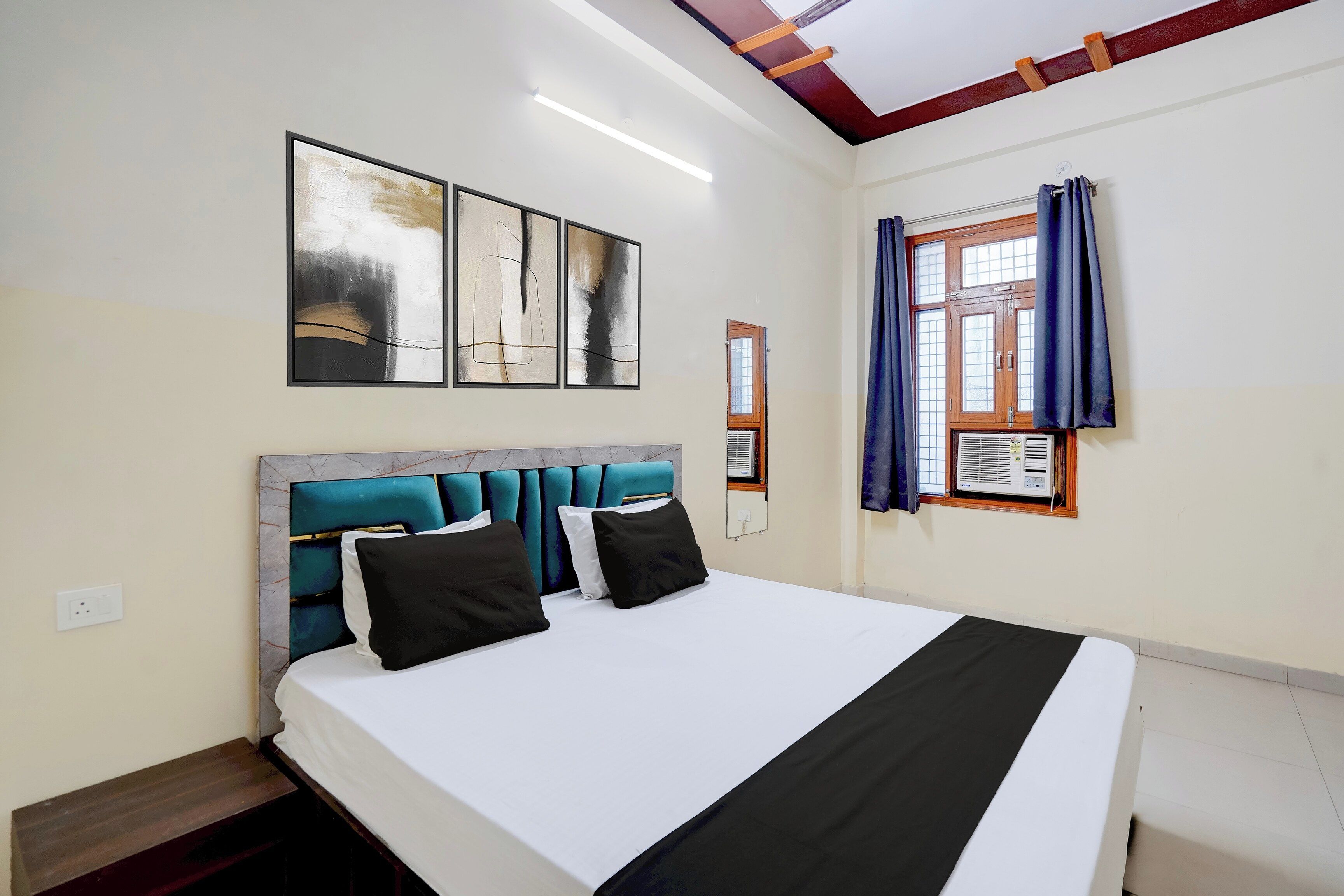 Una habitación de hotel con cama, cabecera, ventana con cortinas y una obra de arte en la pared.