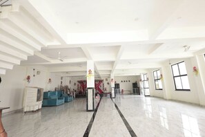 A spacious hall with a high ceiling, marble flooring, and a stage area with floral decorations. - Hotel O Meadows (Mandhana)