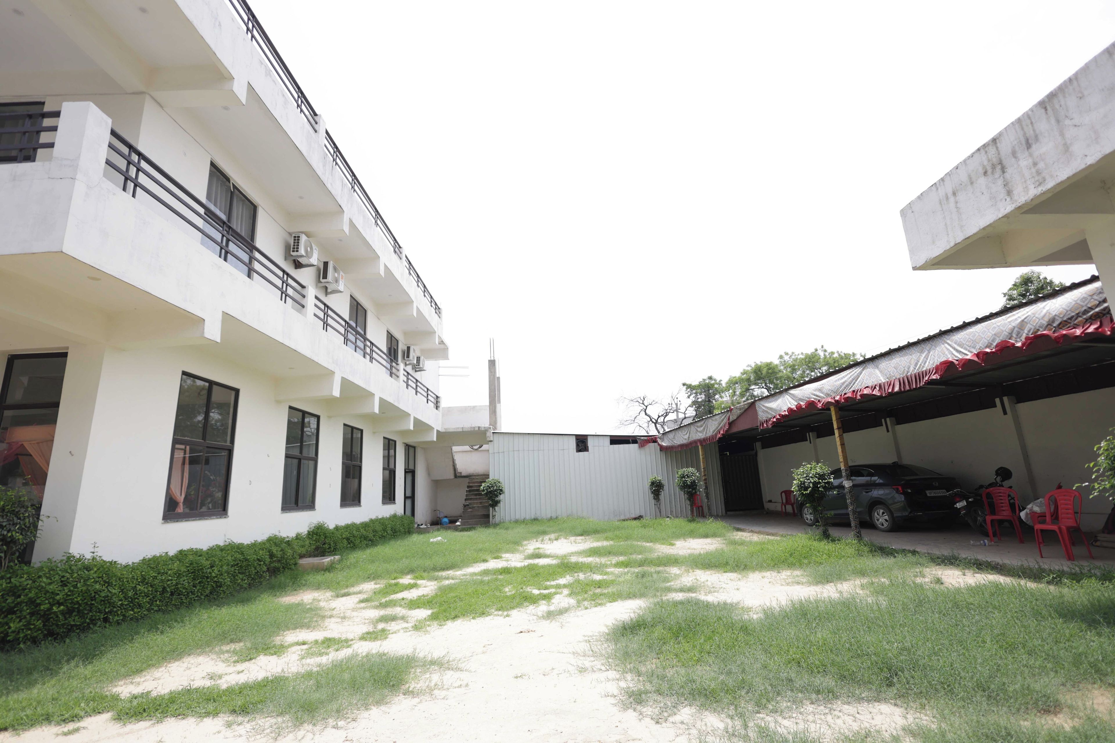 A courtyard with a building on one side and a covered area on the other. There are steps leading to a balcony, and a car is parked under a covered area.