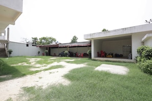 A residential area with a covered outdoor seating area, a car parked inside, and a building with a concrete exterior. - Hotel O Meadows (Mandhana)