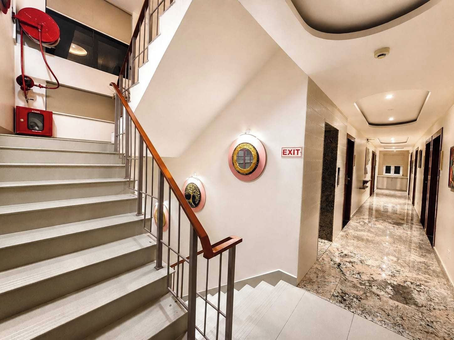 A hotel interior with a staircase, an exit sign, and a hallway leading to a room.