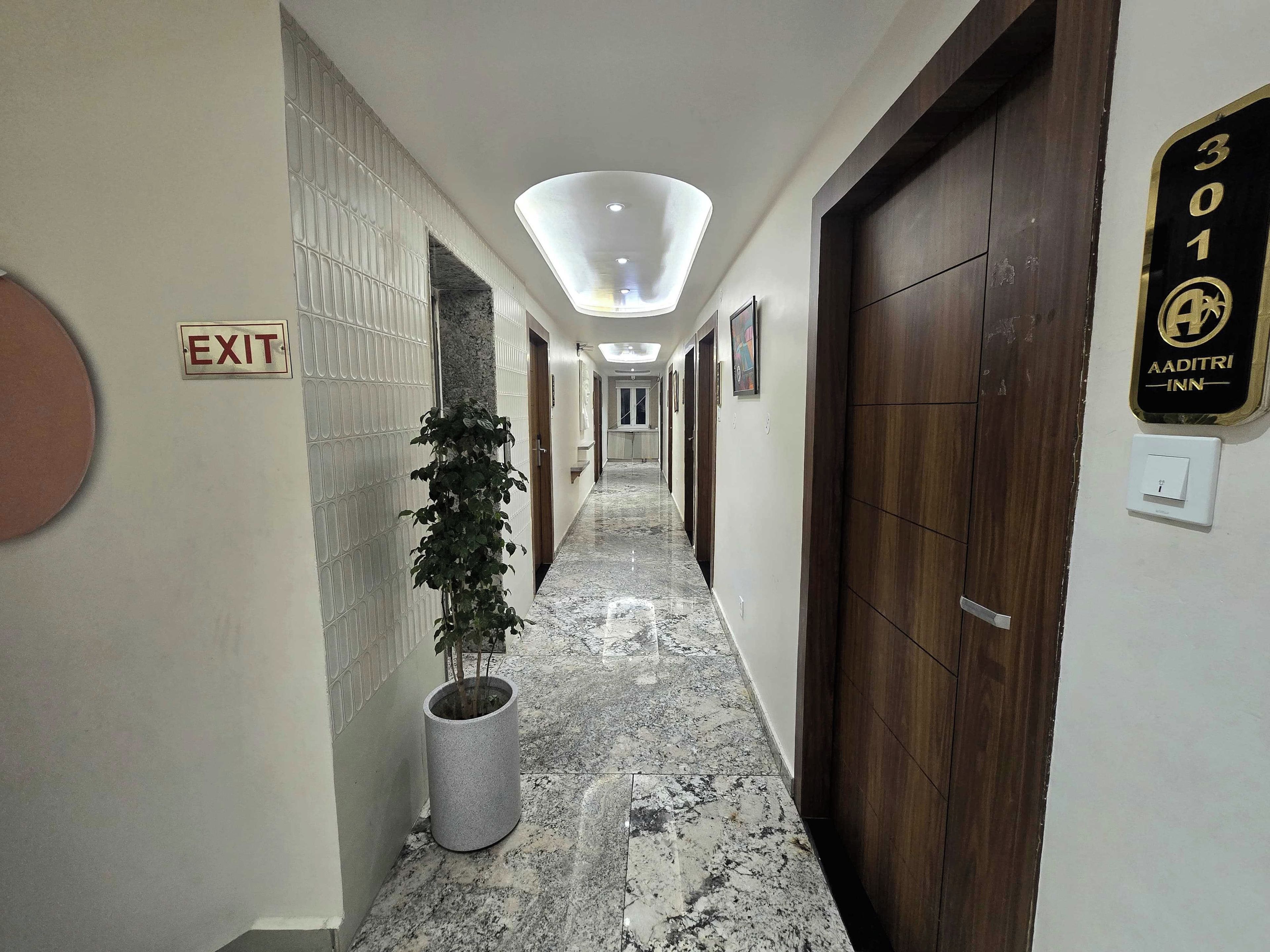 A hotel corridor with an exit sign, a potted plant, a marble floor, and a door with a sign indicating room number 301.