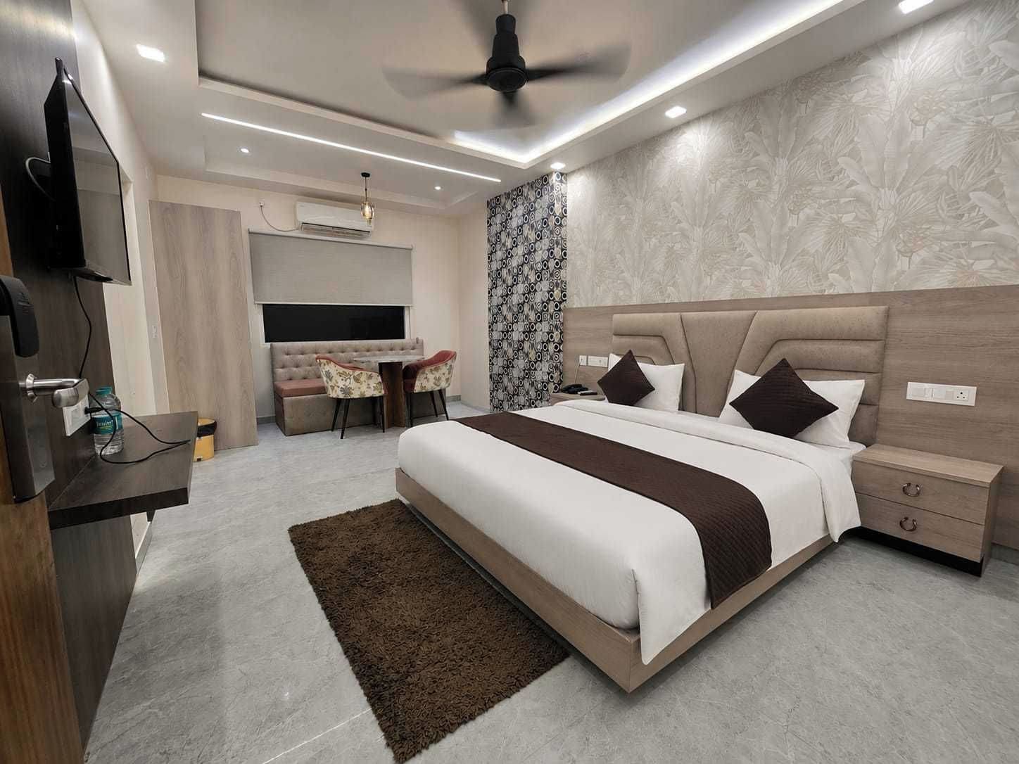 A modern hotel room with a bed, bedside tables, a desk with chairs, a television, and a ceiling fan.