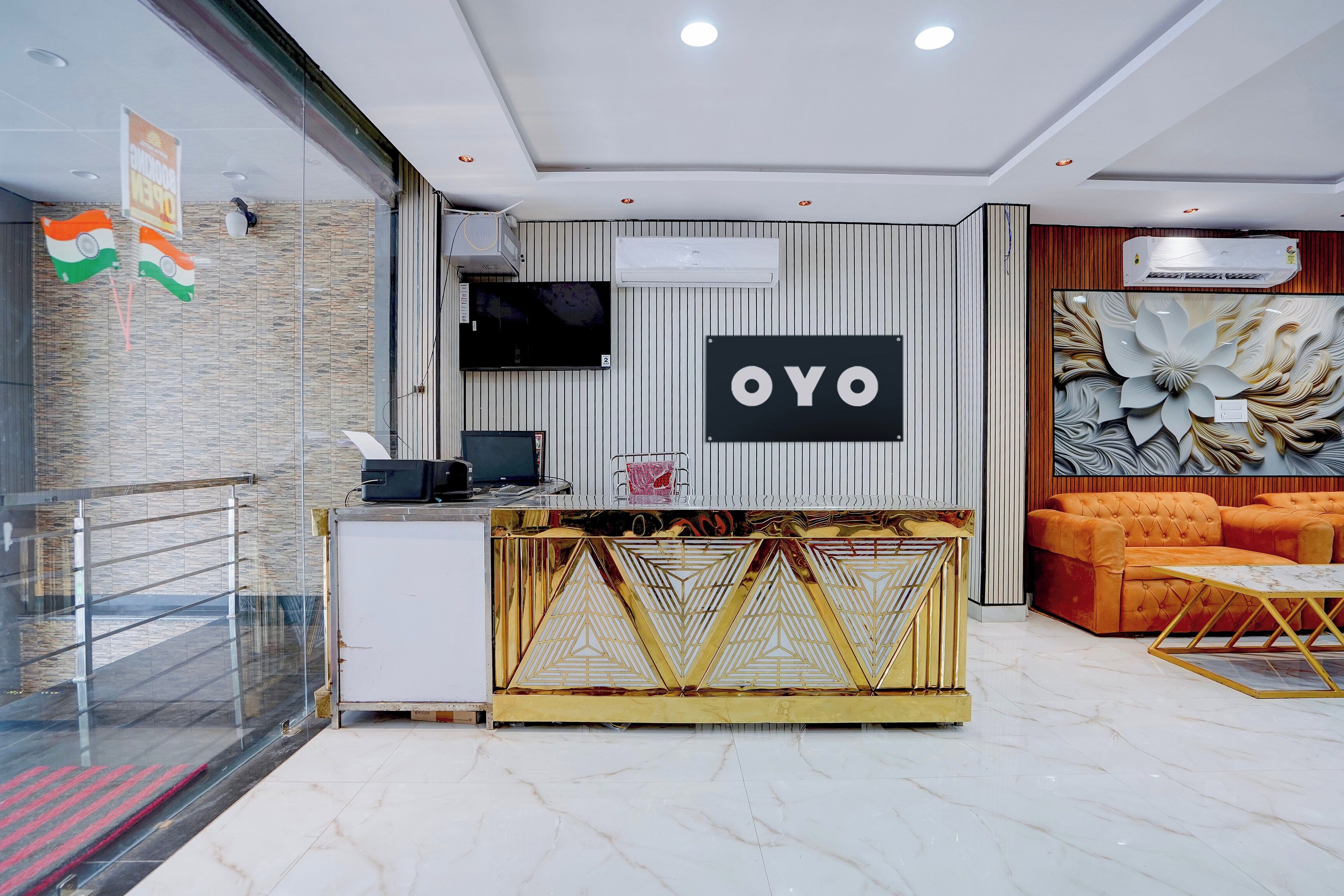 A reception area with a modern design, including a reception desk, a flat-screen TV, and a seating area with a sofa and a decorative wall.