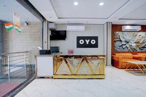 Un área de recepción con diseño moderno, que incluye un mostrador de recepción, un televisor de pantalla plana y un espacio de estar con un sofá y una pared decorativa.