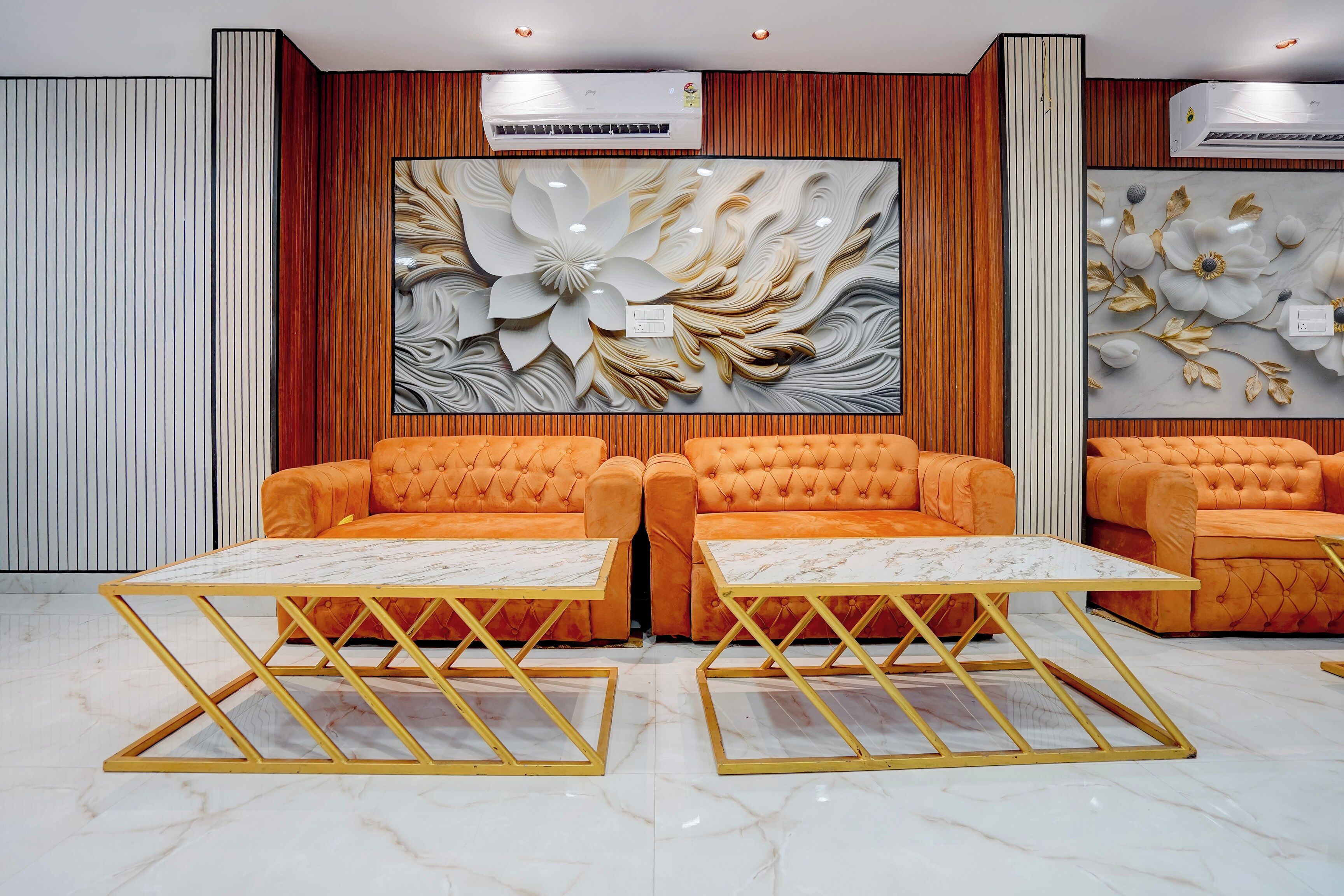 A lobby with two orange sofas and matching tables, a large floral wall mural, and vertical wooden paneling.