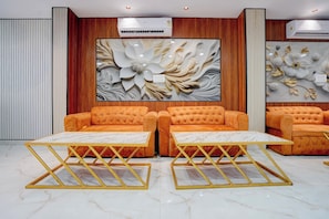 Eine Lobby mit zwei orangefarbenen Sofas und passenden Tischen, einem großen Blumenwandbild sowie vertikaler Holzverkleidung.