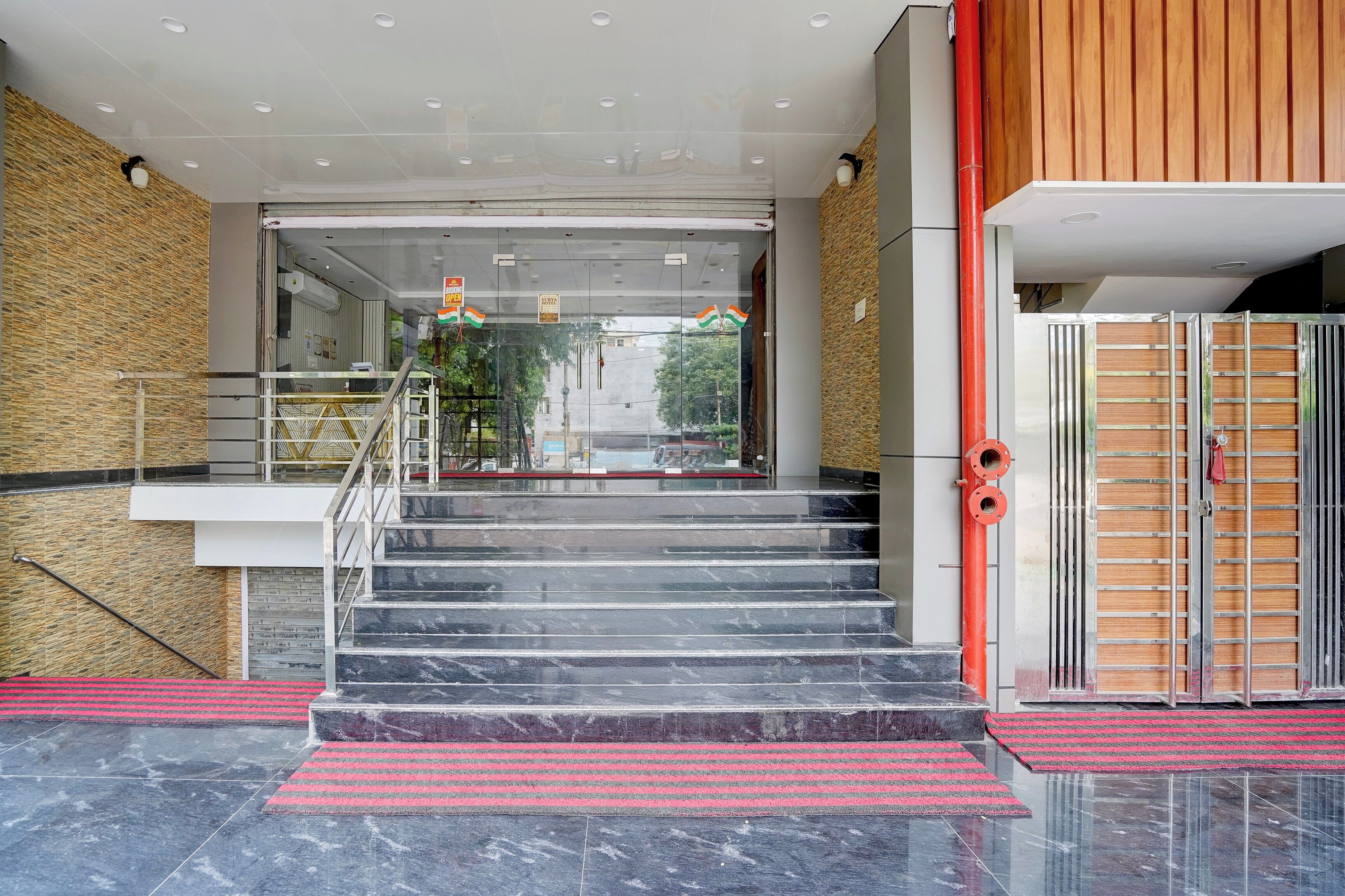 A hotel entrance with a glass door, a staircase, and a red mat leading to the stairs.