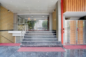 Entrada d'un hotel amb una porta de vidre, una escala i un estriat vermell que hi mena.