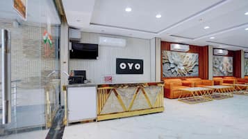 A hotel reception area with a modern design, featuring a reception desk, a large wall-mounted sign, and a seating area with orange sofas.