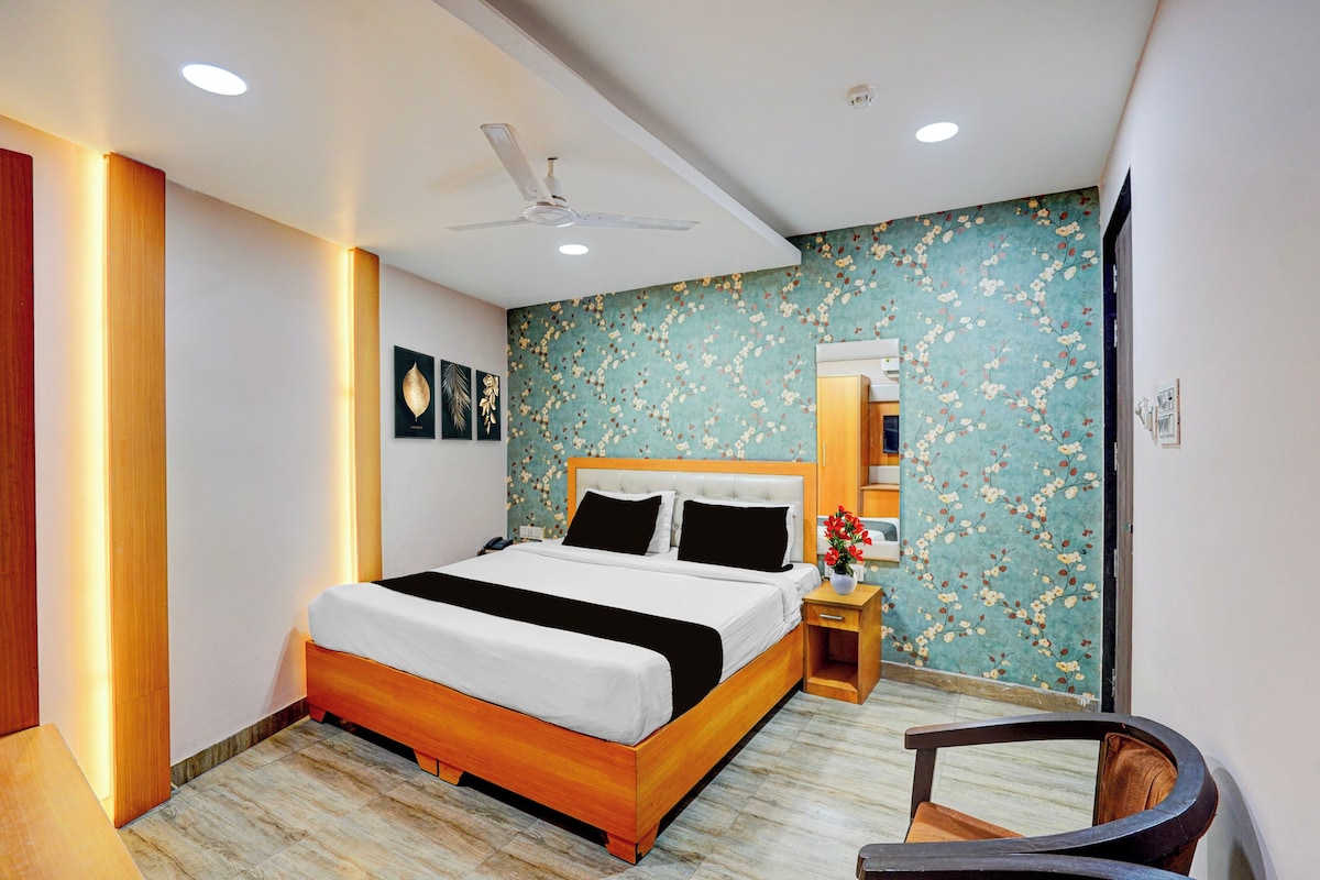 Een hotelkamer met een bed, nachtkastje, stoel, spiegel en bloemenbehang.