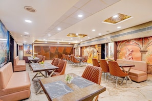 Een restaurant met meerdere eettafels en stoelen, een plafond met inbouwverlichting en decoratieve muurschilderingen.