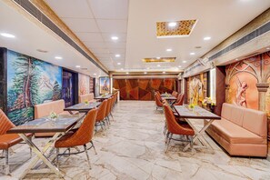 A restaurant with a long counter, cushioned seating, and a mural on the wall. - Townhouse HOTEL THE ROYAL ORCHID (Kanpur)