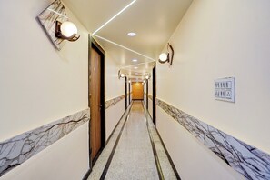 A hotel hallway with marble flooring, wall-mounted lights, and a door on the left. - Townhouse HOTEL THE ROYAL ORCHID (Kanpur)