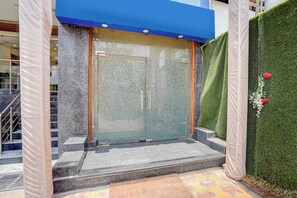 A building entrance with a glass door, a blue awning, and a green hedge. - Townhouse HOTEL THE ROYAL ORCHID (Kanpur)