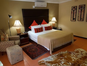 Una habitación de hotel con una cama, dos lámparas de noche, un mesita de noche, una silla, un tapete estampado y un tapete de cuero.