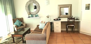 Una sala de estar con un sofá, una silla, un escritorio con silla, un espejo redondo y un tapiz de pared estampado.