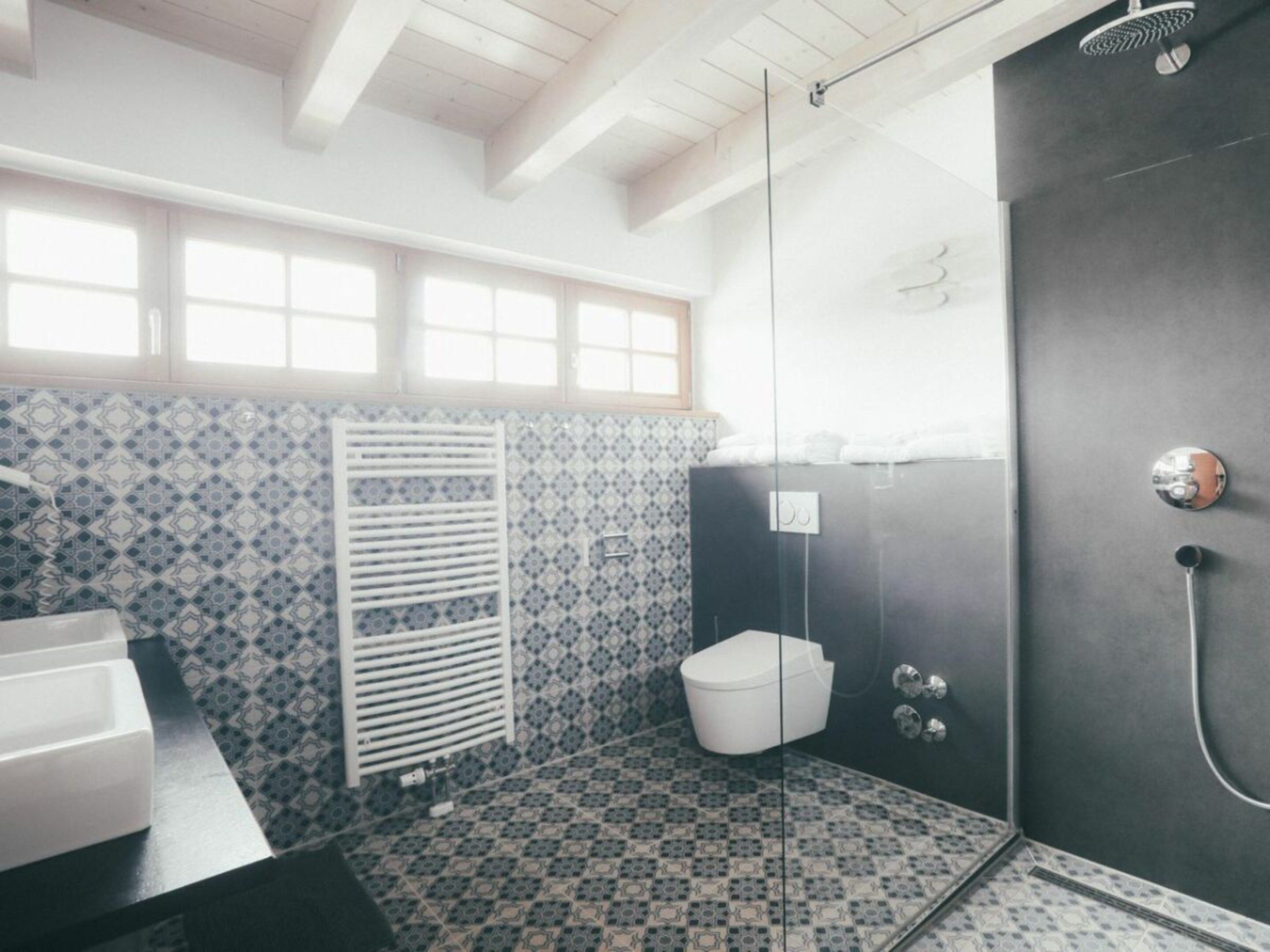 A bathroom with patterned tiles, a white towel rack, a glass shower enclosure, and a toilet.