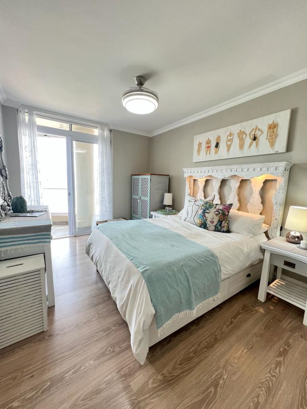 A bedroom with a bed, a nightstand, a dresser, a ceiling fan, and a window with curtains.