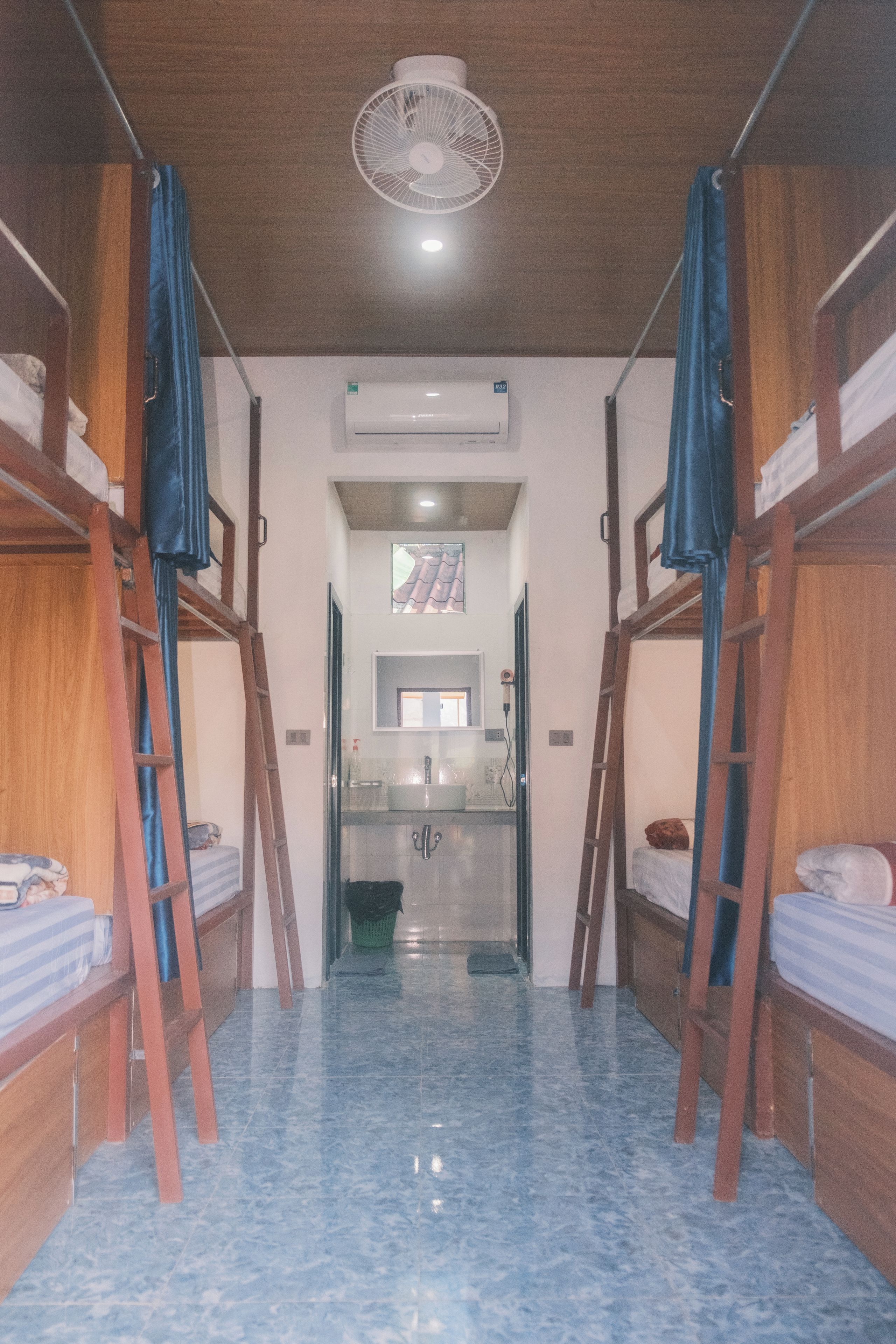 A room with bunk beds, a bathroom with a sink and mirror, and an air conditioning unit on the wall.