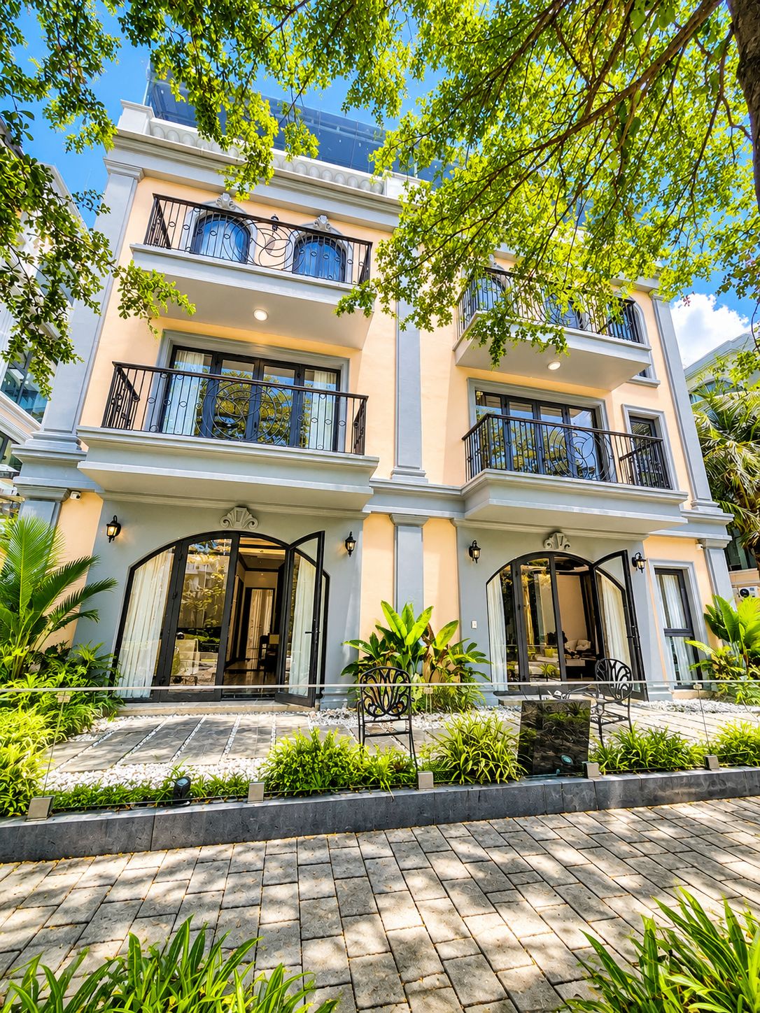 A multi-story building with balconies, large windows, and a paved entrance area with plants.
