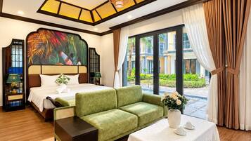 A hotel room with a bed, a green sofa, a small table with a vase, and a view of the outside.