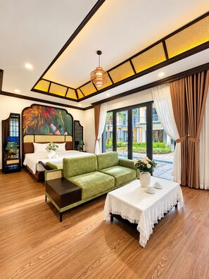 Quarto de hotel com cama, um sofá verde, uma mesinha com um vaso e vista para o exterior.