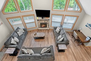 A spacious living room with a stone fireplace, large windows, and a flat-screen TV. - 9BR Lake Harmony Luxury/Hot Tub, Deck Bar & Zero Gravity Massage Chairs (Lake Harmony)