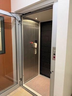 An elevator with a metallic interior, a red emergency stop button, and a white handset. - Brisbane City View Mansion | Pool & Cinema (Bardon)