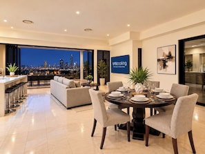 A modern dining area with a round table set for six, a sofa, and a city view. - Brisbane City View Mansion | Pool & Cinema (Bardon)