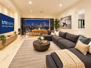 A modern living room with a sofa, coffee table, and a city view. - Brisbane City View Mansion | Pool & Cinema (Bardon)