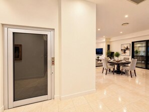 Un intérieur moderne avec un coin repas comprenant une table ronde et des chaises, une porte vitrée donnant sur un couloir et une cuisine visible à travers une cloison en verre.